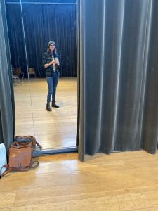 Ali taking a mirror selfie in a rehearsal hall floor to ceiling mirror.