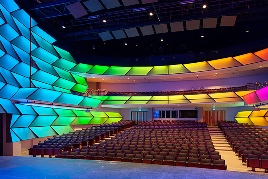 From the stage, we gaze out over the empty seats of the Lyric Theatre in Meridian Arts Centre. Above and beside the seats are geometric, backlit panels in every colour of the rainbow, displaying the programmable lighting feature.