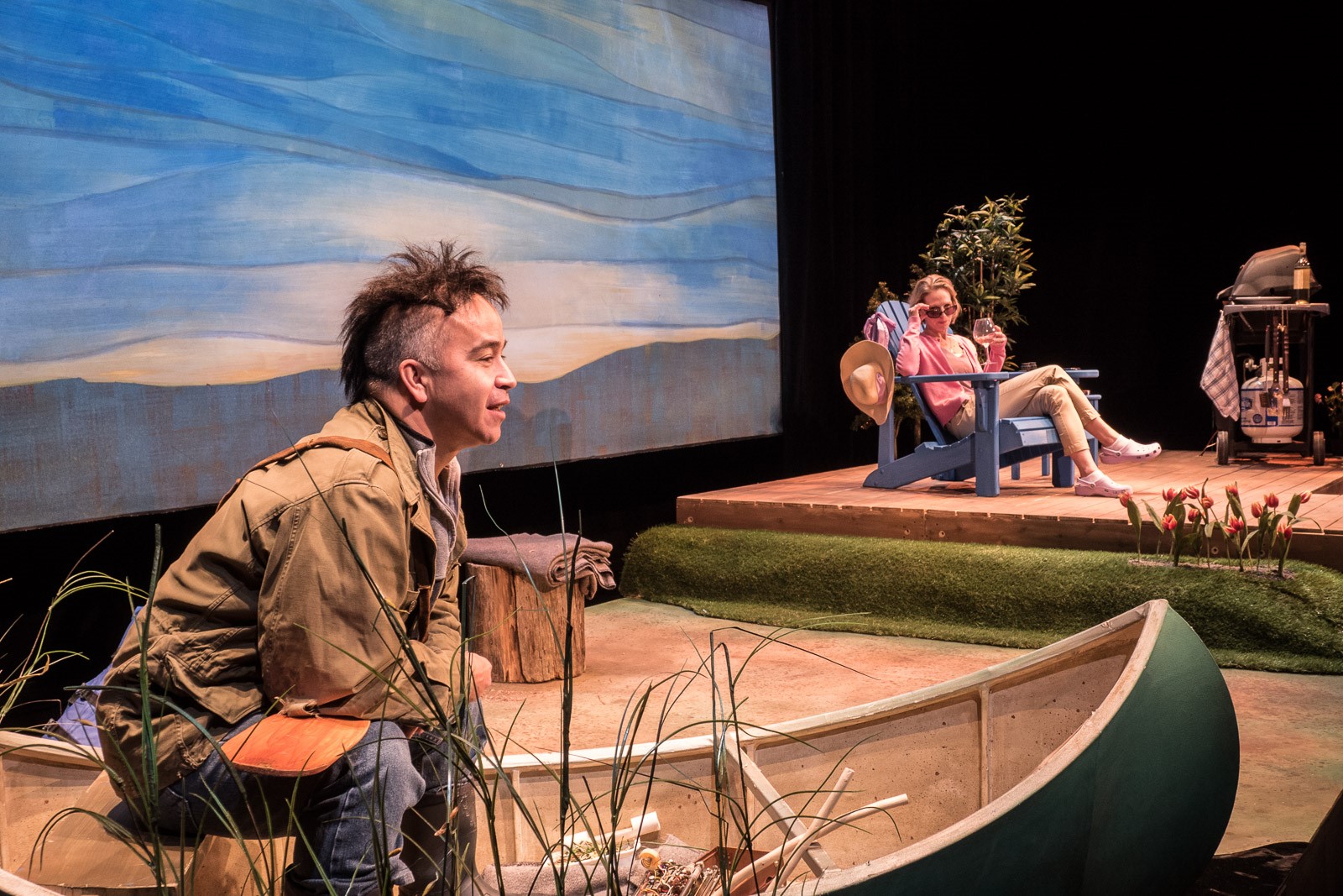 A production still from Tarragon Theatre's touring production of Drew Hayden Taylor's "Cottagers and Indians" - actor Herbie Barnes perches on the edge of a canoe while Philippa Domville watches from a lounge chair.