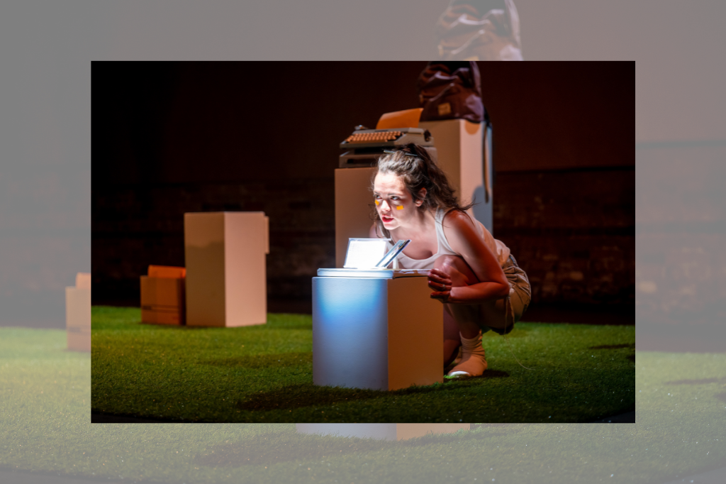 Haley McGee crouches onstage behind a white pedestal. Below her is a carpet of astroturf, and other pedestals can be seen behind her, displaying a variety of objects. Her face is illuminated by the light reflecting off a mixtape in front of her. There are small orange sticky notes on her face below each eye, and she wears a white tank top and shorts, with her long brown hair pulled into a ponytail.