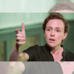 The banner image for Intermission's review of Girls & Boys, a Here for Now Theatre production in association with Crow's Theatre. The image shows Fiona Mongillo, Here for Now's AD and the sole performer in the production, wearing a green collard jumpsuit. She stares past the camera imploringly, one hand raised in front of her as though asking an important question.