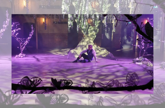 Man in play costume sitting on stage beneath fake tree, in purple lighting