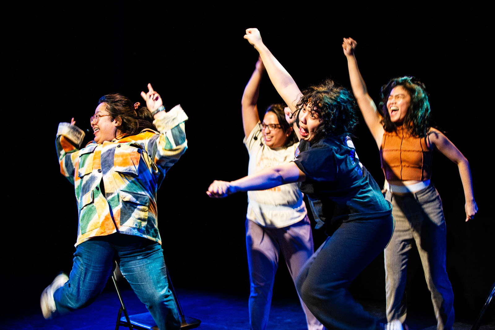 The cast of Tita Jokes, a Tita Collective Production, perform in the Ottawa Fringe. The four performers wear bright colours and stand on stage with their arms raised as if in triumph.