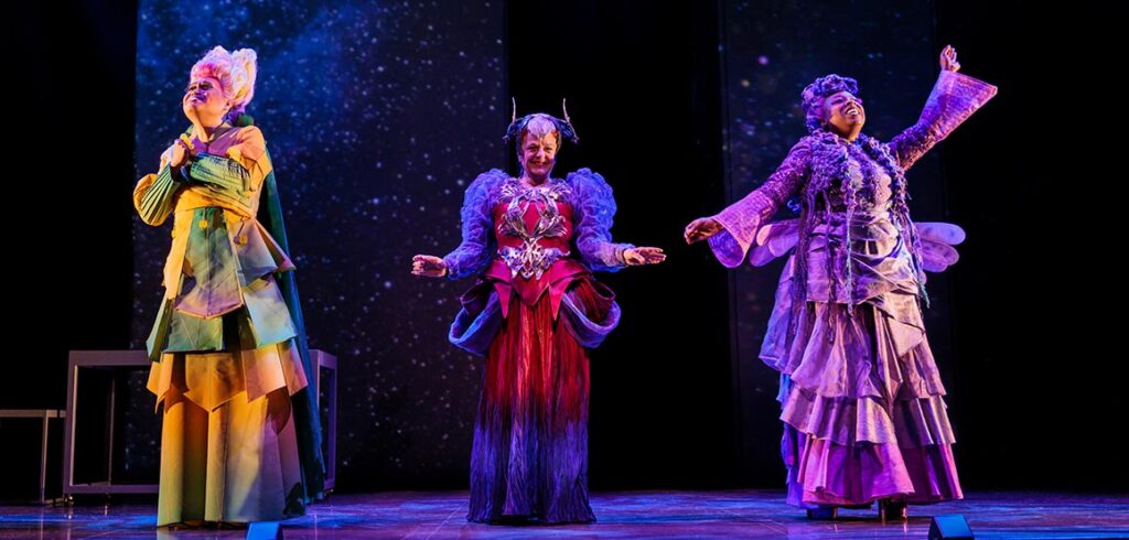 From left: Nestor Lozano Jr., Kim Horsman, and Khadijah Roberts-Abdullah in A Wrinkle in Time at Stratford. The three wear long, colourful dresses: Lozano's in yellow and green, Horsman's in red and blue, and Roberts-Abdullah's in purple and silver. Photo by David Hou