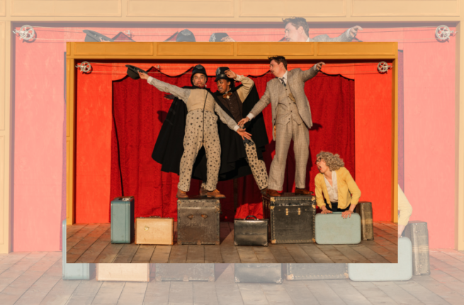 The cast of The 39 Steps perform on a bright orange stage franed by red curtains. They are dressed in period garb in tones of beige brown, and yellow, and balance precariously on a collection of suitcases. Photo by Sarah Kirby.