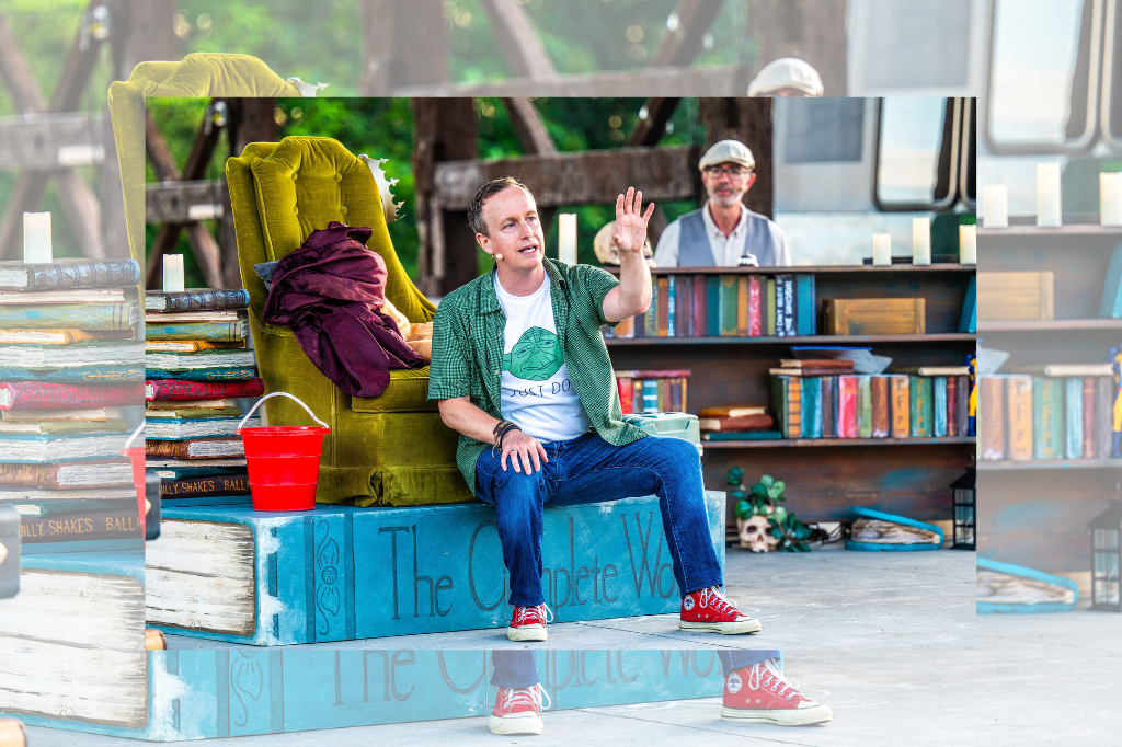 Jeremy Smith sits atop a massive volume of Shakespeare's completed works. He wears a yoda t-shirt with a green button-down, jeans, and red Converse sneakers. His arm is raised as though speaking dramtically. Around him is a cluttered stage: books, figurines, a chartreuse velvet "throne," and a red plastic pail surround him. Behind him, Tom Lillington is just visible behind a piano. Original image by Dahlia Katz.