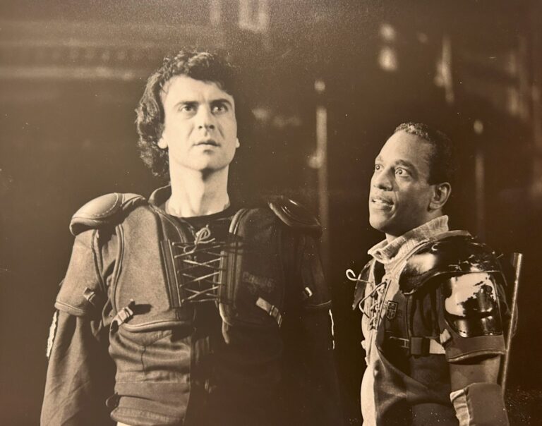 A sepia-toned image from the 1992 production of Edward IV at Dream in High Park. Two armour-clad performers are pictured, one staring upwards with determination, the other speaking to the first with apparent urgency.