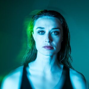 Portrait of a woman, looking straight ahead with melancholy expression, cast in blue light