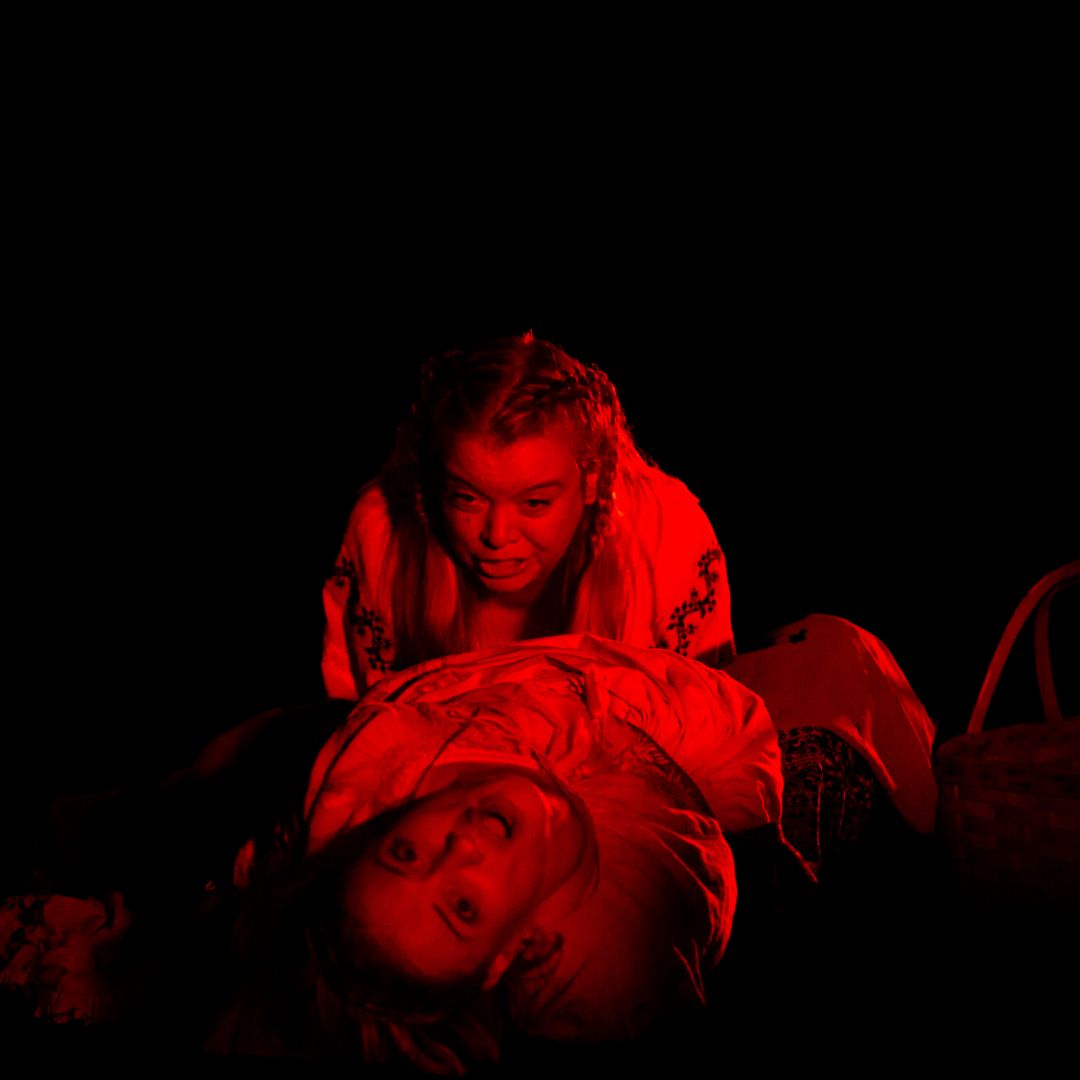 Two women are screaming on the ground outside, cast in a red light.