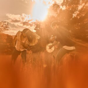 Two people dancing and playing music in a field. Orangey filter over photo.