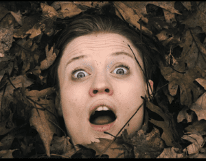 An image of a woman screaming, surrounded by fallen leaves
