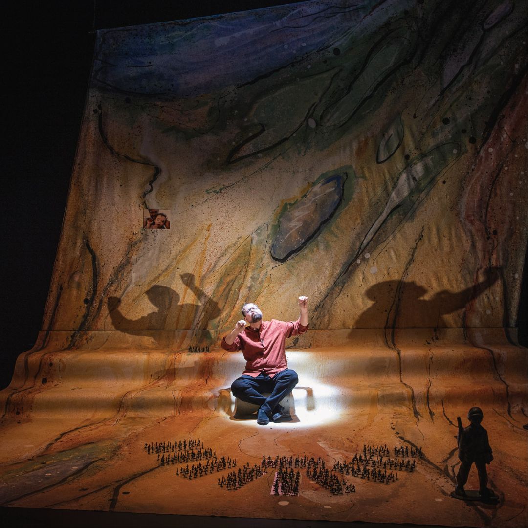 Itai Erdal, sitting against a desert-ish backdrop. Toy soldier figurines surround him.