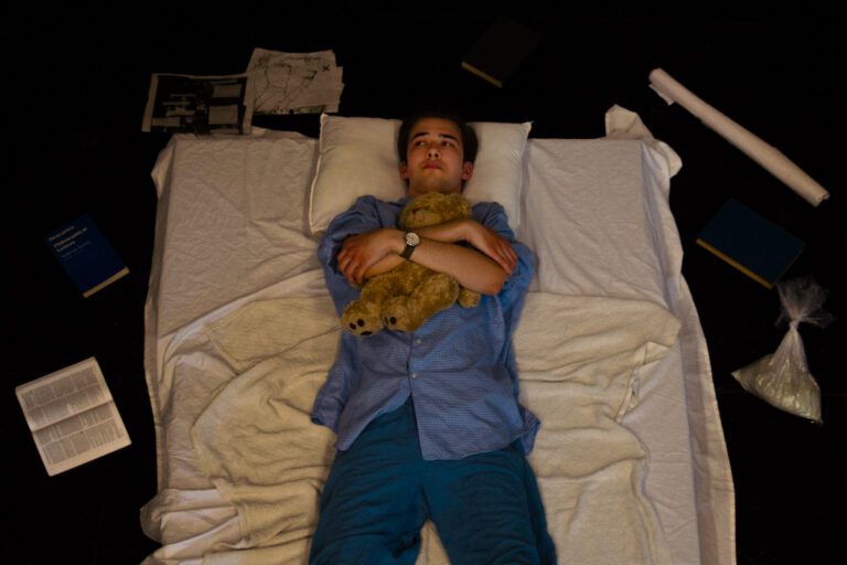 Gabriel (Charles Ford) lying on his bed, surrounded by the objects of his consciousness. 