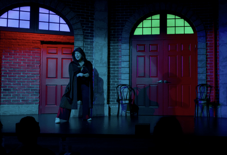 Janelle crouches dressed as a witch in dim lighting.