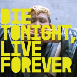 A person with short blond hair and a metallic jacket presses their fingers against their mouth with their eyes closed. Large yellow text reads “DIE TONIGHT, LIVE FOREVER.”
