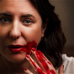 Image of a woman looking intently into camera with blood on her fingers.